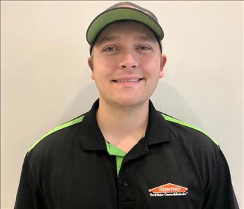 Male with hat, wearing a black SERVPRO shirt with green on shoulders and button area.