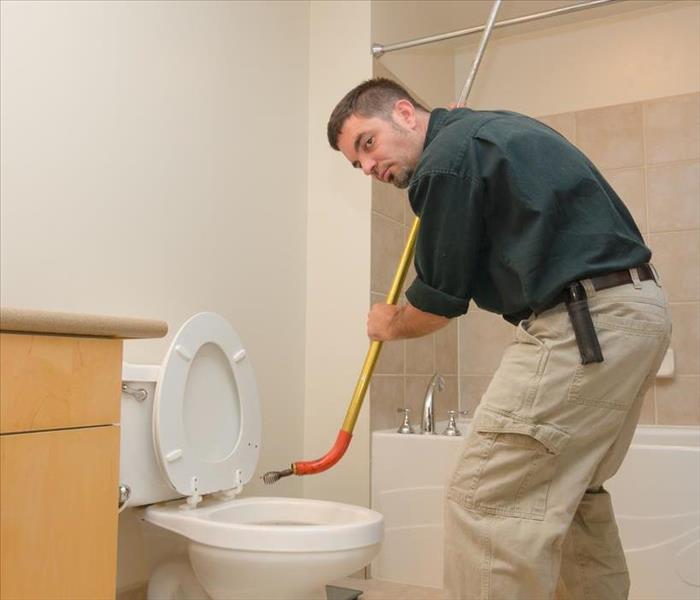 A plumber unclogging a toilet with a plumber's snake